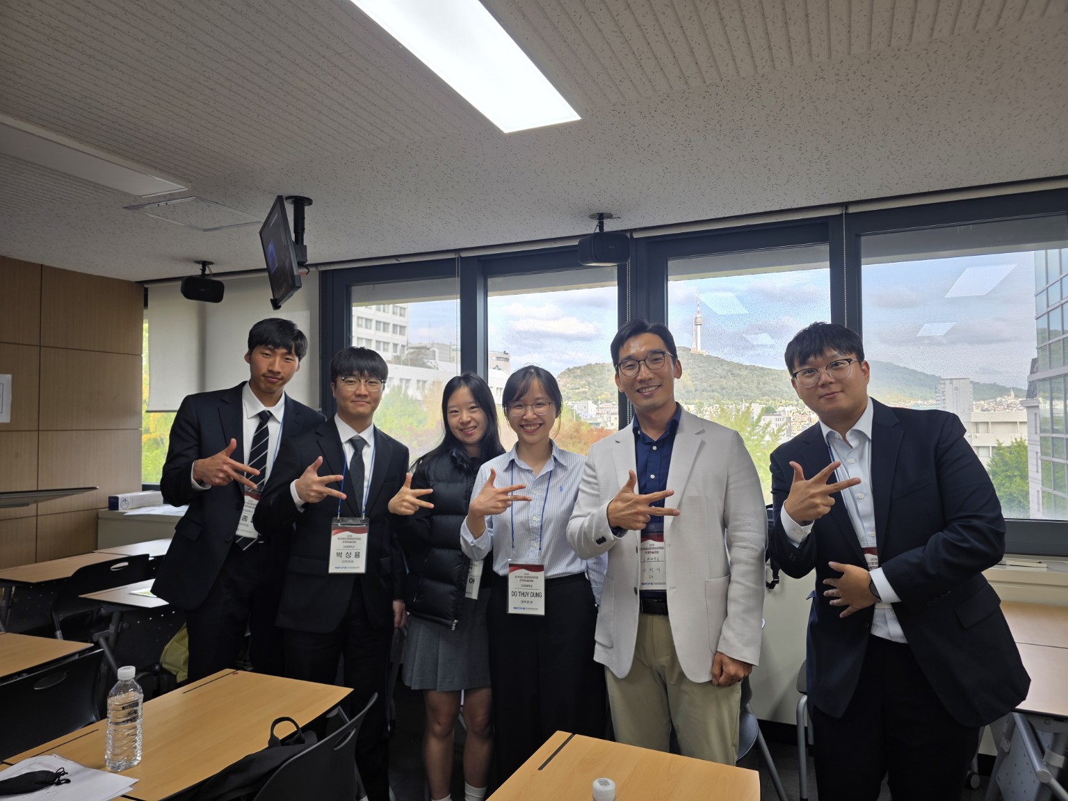 Hyun Seok Lee and five student presenters making K hand gestures at the 2026 KOPOMS Fall Conference.