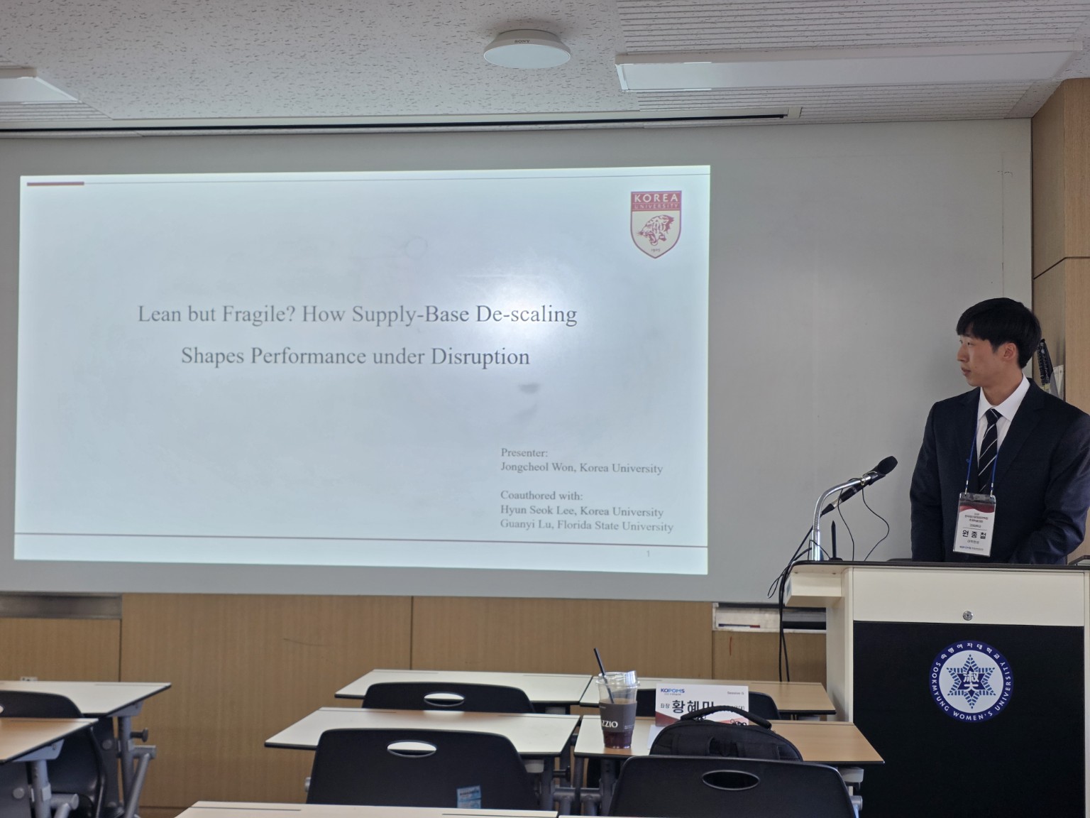 Jongcheol Won at a lectern beside his supply-base de-scaling presentation slide.